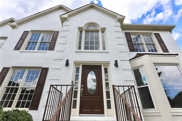 White brick exterior featuring dark shutters, a decorative arched window, and a bay window