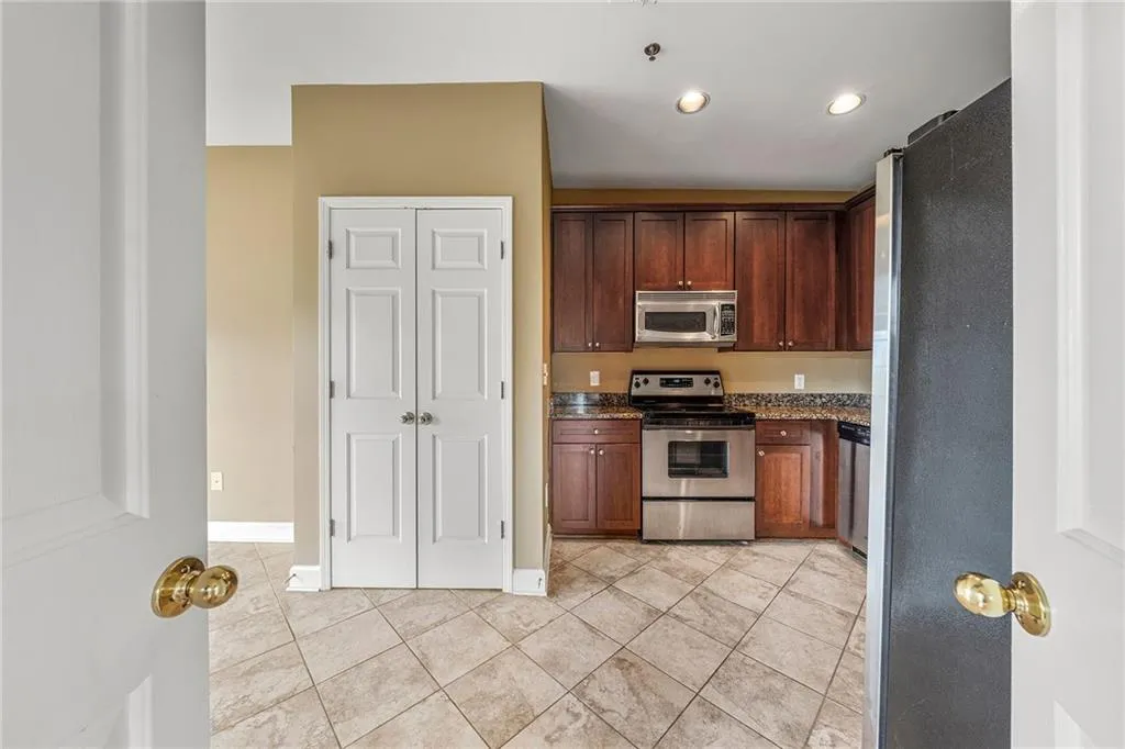 Kitchen featuring appliances with stainless steel finishes, light tile patterned flooring, dark stone counters, recessed lighting, and dark brown cabinetry