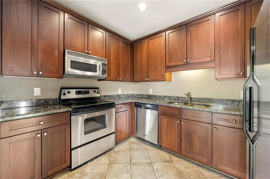 Kitchen featuring appliances with stainless steel finishes, dark stone counters, light tile patterned flooring, recessed lighting, and brown cabinetry