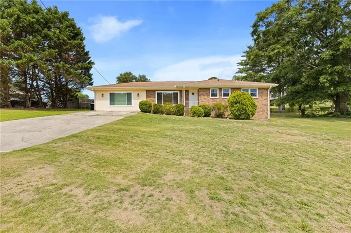 Brick and stucco exterior with a hip roof, featuring a concrete driveway and mature perimeter trees