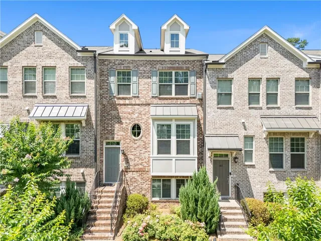 Three-story townhome with a brick facade featuring a central bay window, multiple dormers, and individual metal awnings over entryways