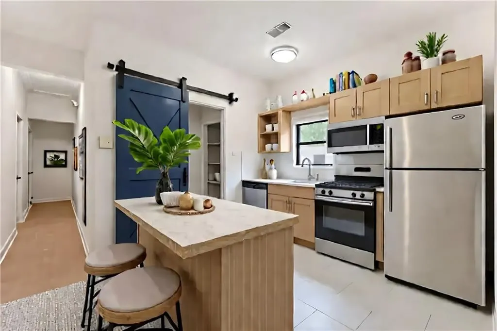 Kitchen featuring light brown cabinetry, stainless steel appliances, light countertops, a barn door, and a breakfast bar area