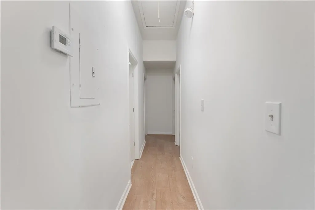 Hall with light wood finished floors, attic access, and electric panel