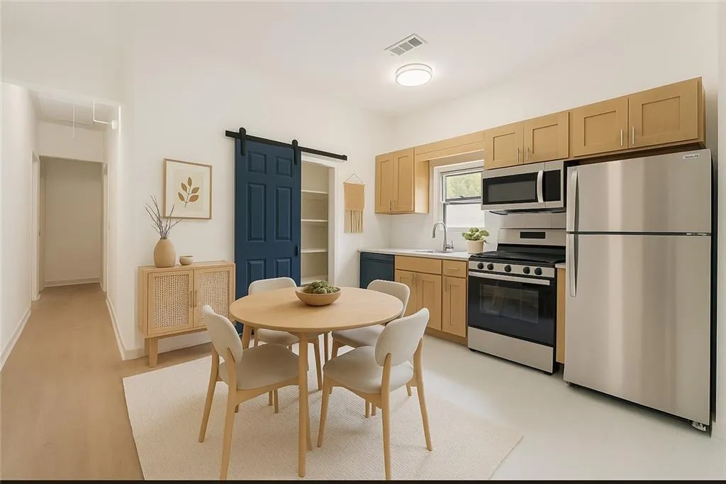Kitchen with a barn door, stainless steel appliances, light brown cabinetry, and light countertops