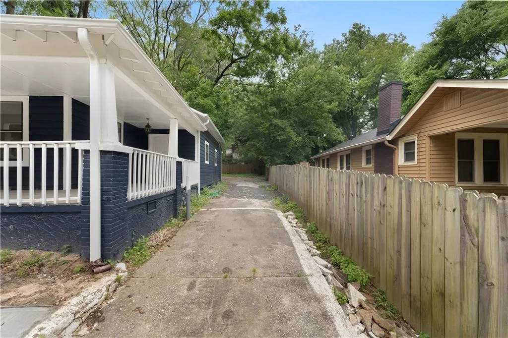 View of side of property featuring a chimney, driveway, a porch, and view of scattered trees