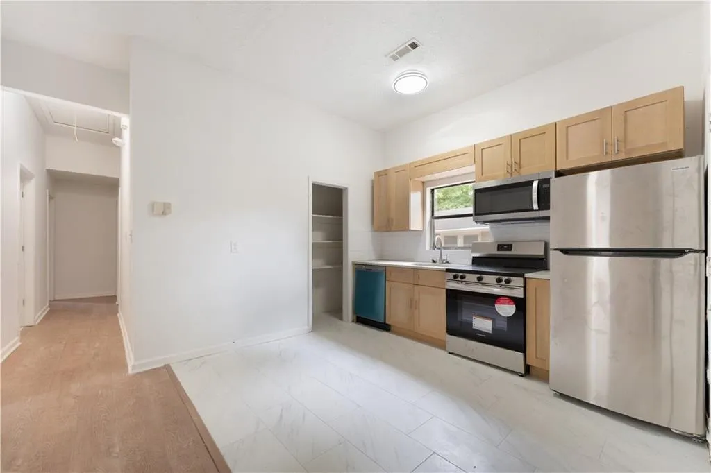 Kitchen with light brown cabinetry, appliances with stainless steel finishes, light countertops, decorative backsplash, and light wood finished floors