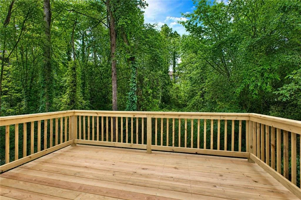 Expansive wood deck with a natural wood finish, featuring classic baluster railing and a backdrop of dense, mature trees