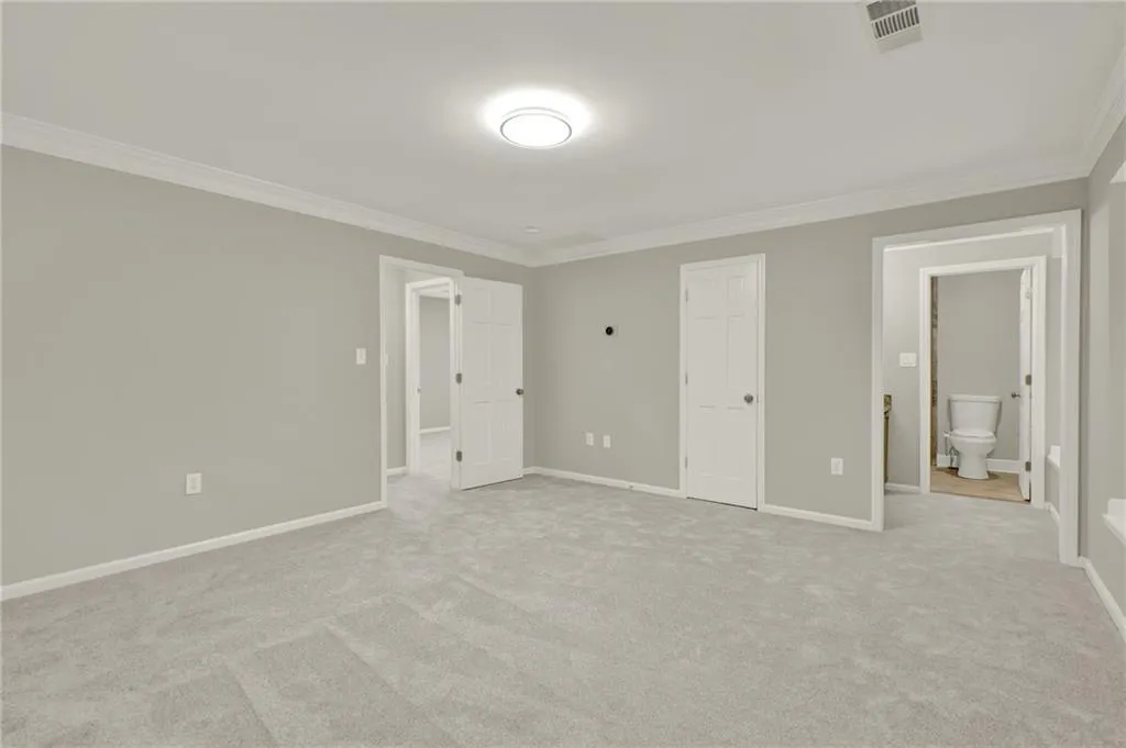 Spacious room featuring light gray wall paint, white crown molding, and plush light gray carpeting