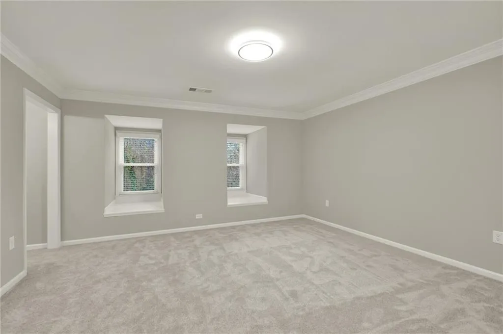 Spacious room featuring light grey carpeting, neutral wall paint, and white crown molding