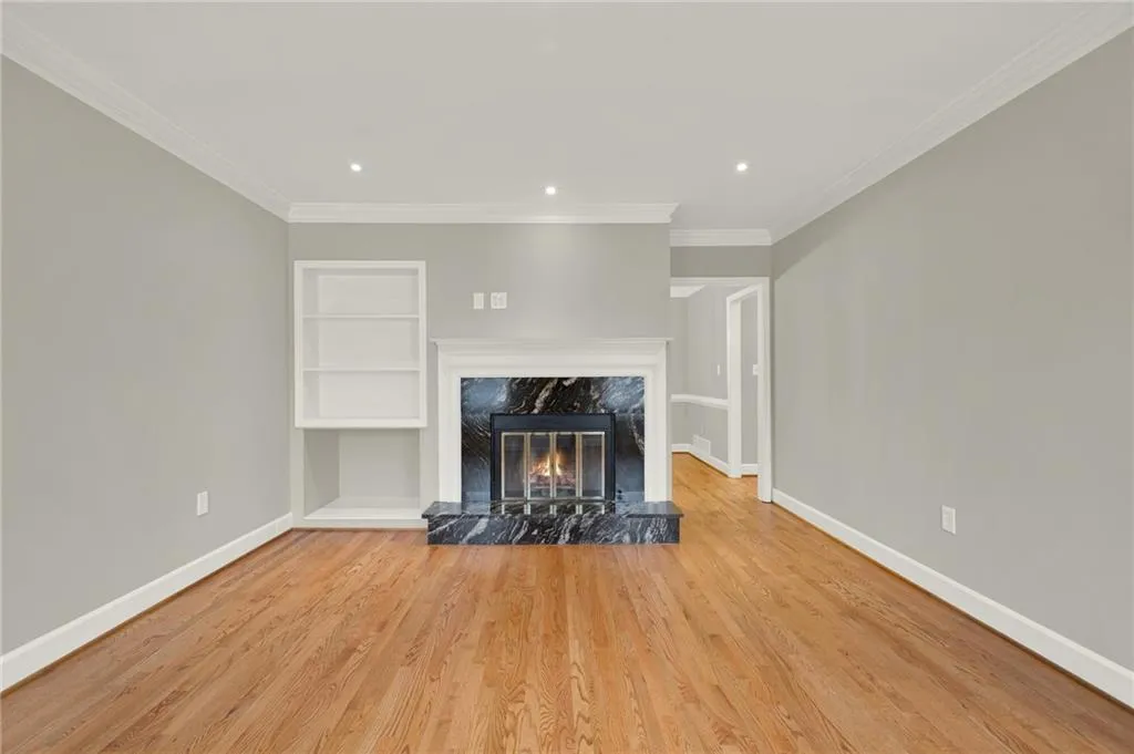 Living area featuring wood-finish flooring, a black marble fireplace surround, a white mantel, and built-in shelving