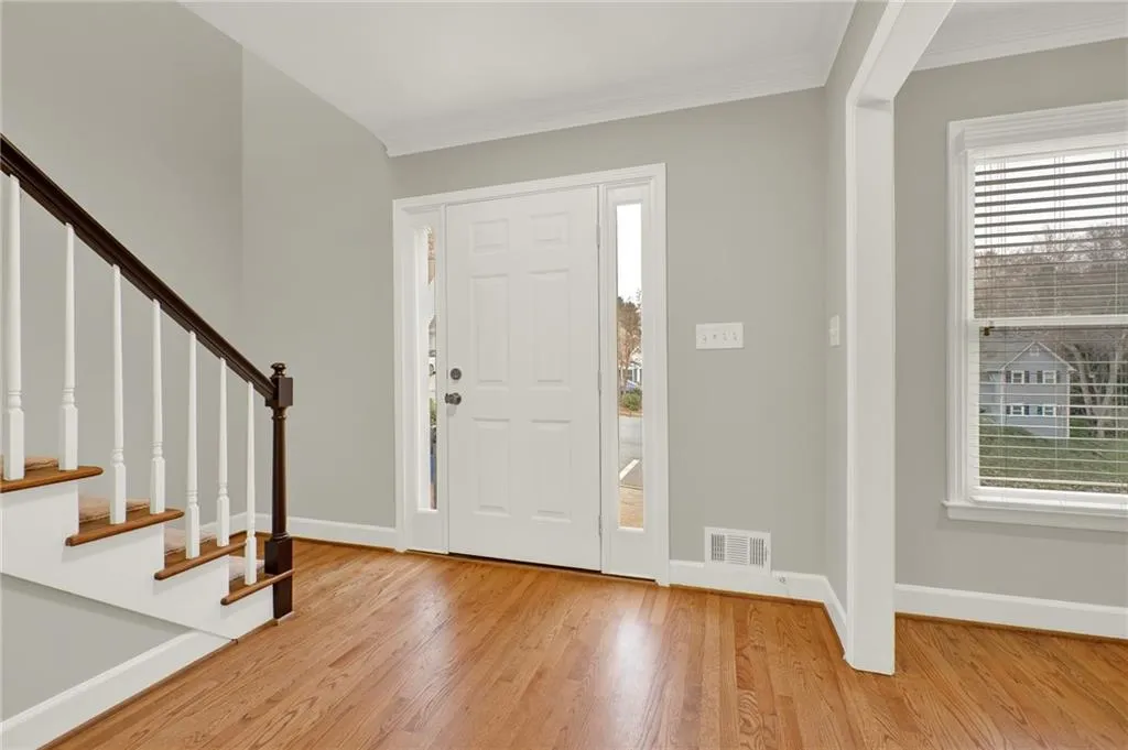 Entry foyer featuring wood-finish flooring, a white paneled entry door with sidelights, a staircase with dark wood handrail and white balusters, and a window with horizontal blinds