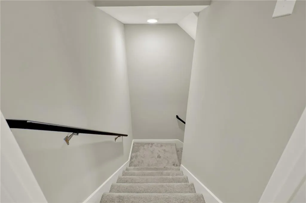 Staircase with light gray carpeted steps, white trim, and a contemporary black handrail