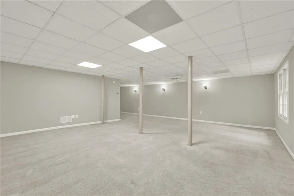 Spacious room featuring light gray walls, plush carpeting, and a drop ceiling with recessed lighting