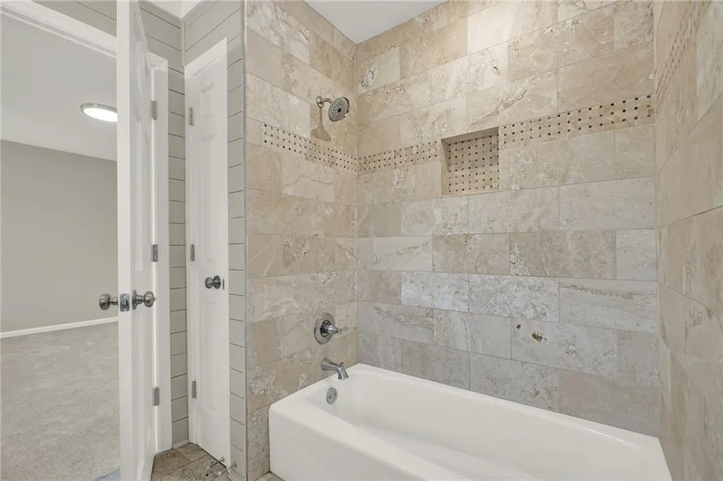 Bathtub with chrome fixtures, full-height stone-look tile surround, and an integrated shower niche