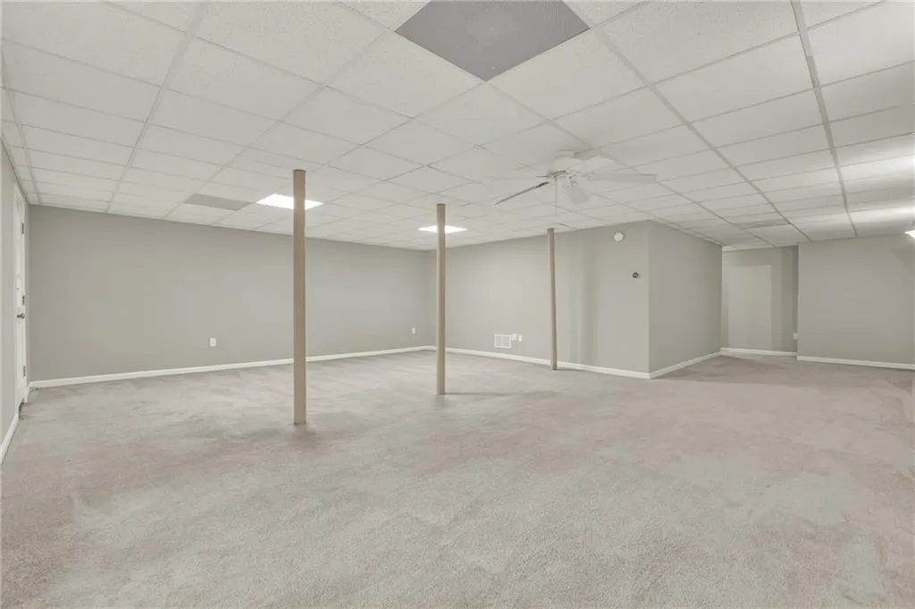Expansive finished lower level featuring light gray carpeting, neutral wall tones, and a drop ceiling with recessed lighting