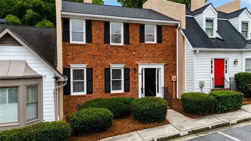 Brick facade townhouse featuring a black front door with white trim, black shutters, and well-maintained shrubbery