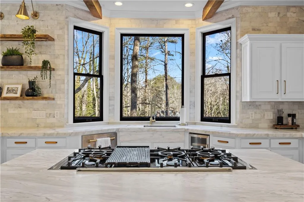 Kitchen featuring white cabinets, decorative backsplash, stainless steel gas stovetop, light stone counters, and open shelves