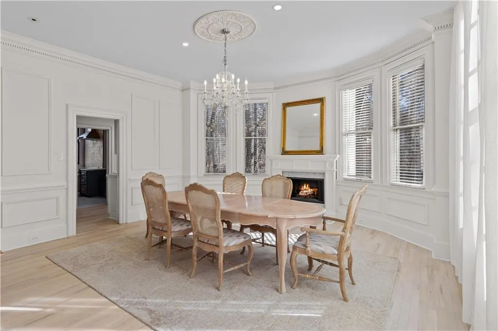 Dining space with a decorative wall, suspended lighting, crown molding, light wood-style floors, and a fireplace