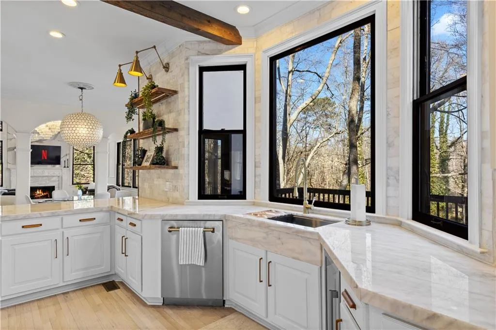 Kitchen with crown molding, light stone countertops, a warm lit fireplace, stainless steel dishwasher, and white cabinets