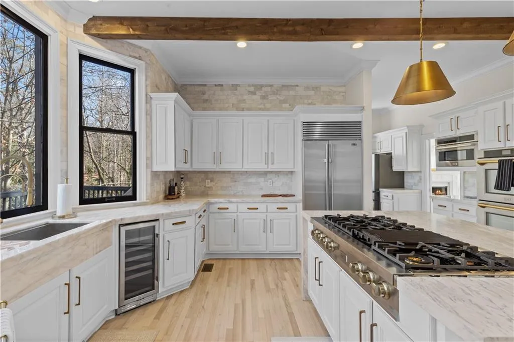 Kitchen featuring ornamental molding, stainless steel appliances, beverage cooler, light wood-style flooring, and white cabinets