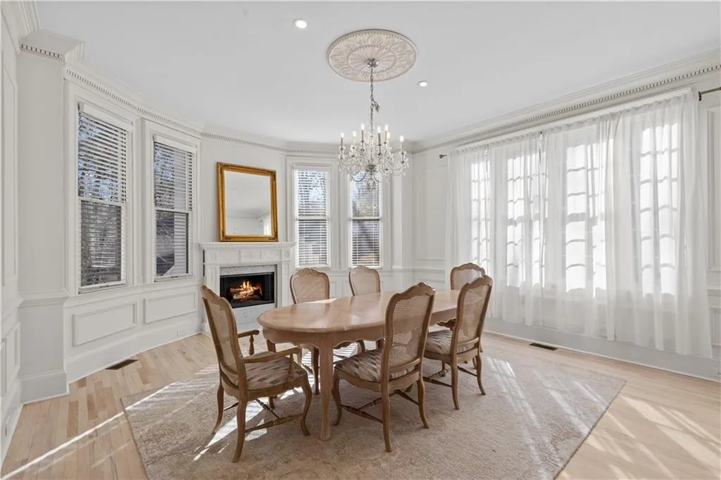 Dining space featuring a premium fireplace, a decorative wall, suspended lighting, light wood-style floors, and ornamental molding