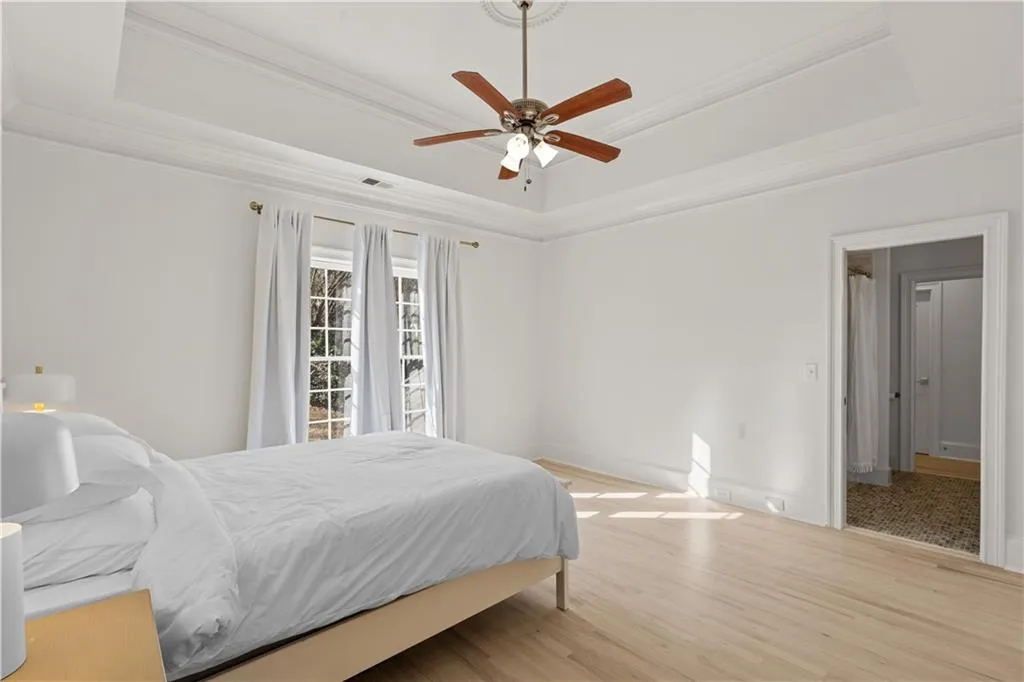 Bedroom with light wood finished floors, ceiling fan, a tray ceiling, and crown molding