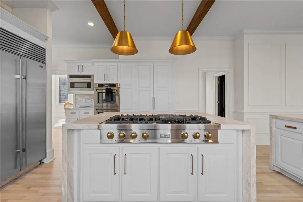 Kitchen with white cabinets, stainless steel appliances, light stone countertops, and crown molding