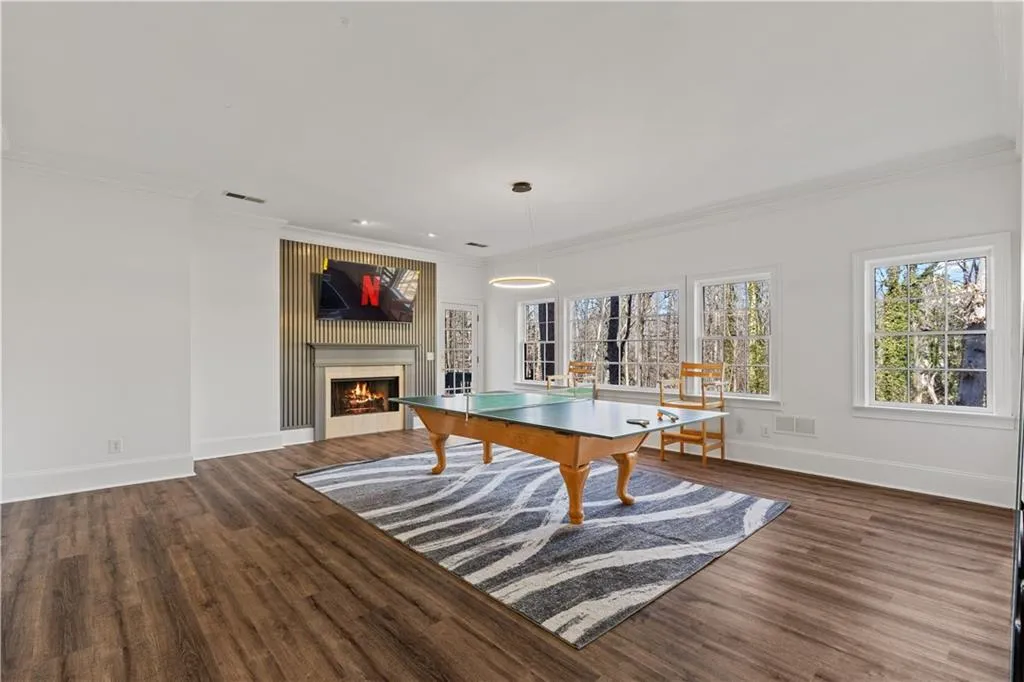 Rec room featuring dark wood-style flooring, ornamental molding, and a large fireplace