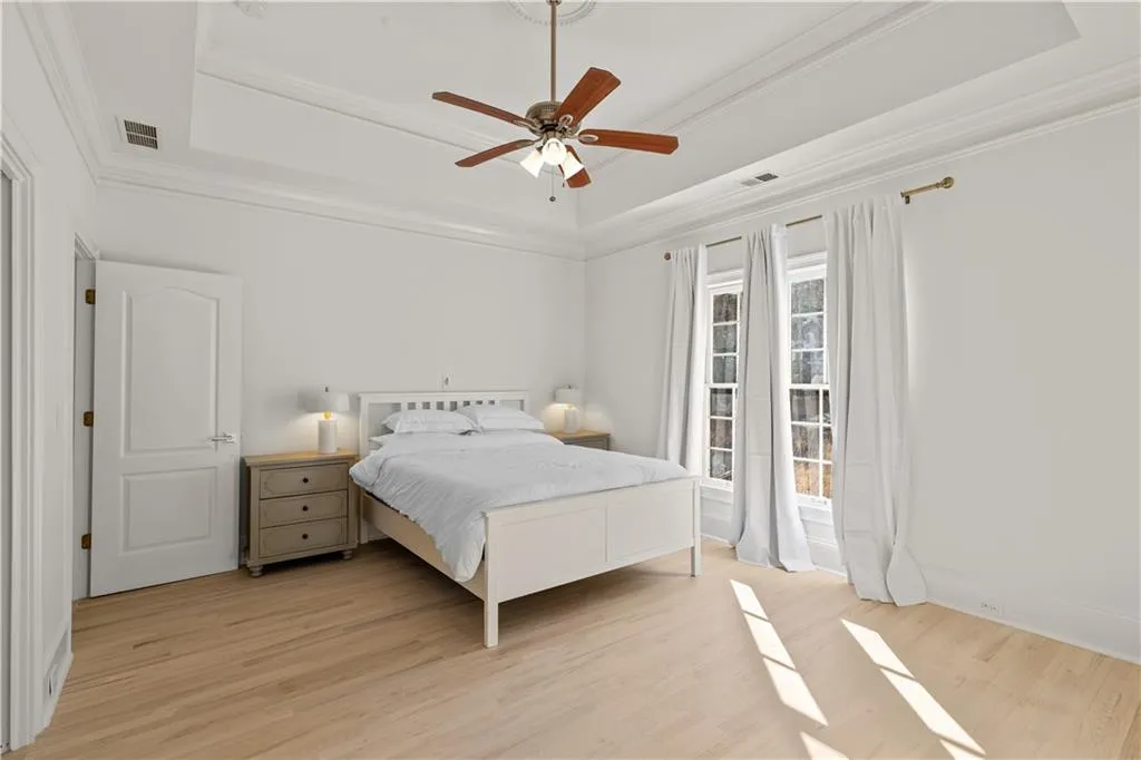 Bedroom with light wood-style flooring, ornamental molding, a tray ceiling, and ceiling fan