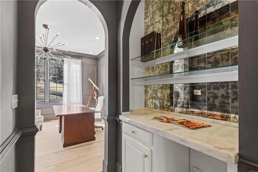 Bar area featuring white cabinets, light wood-style flooring, hanging lights, arched walkways, and backsplash