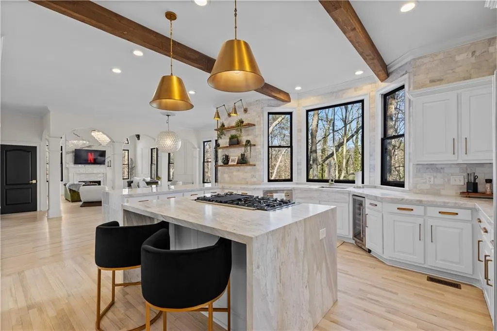 Kitchen featuring light stone counters, open floor plan, tasteful backsplash, hanging light fixtures, and white cabinets