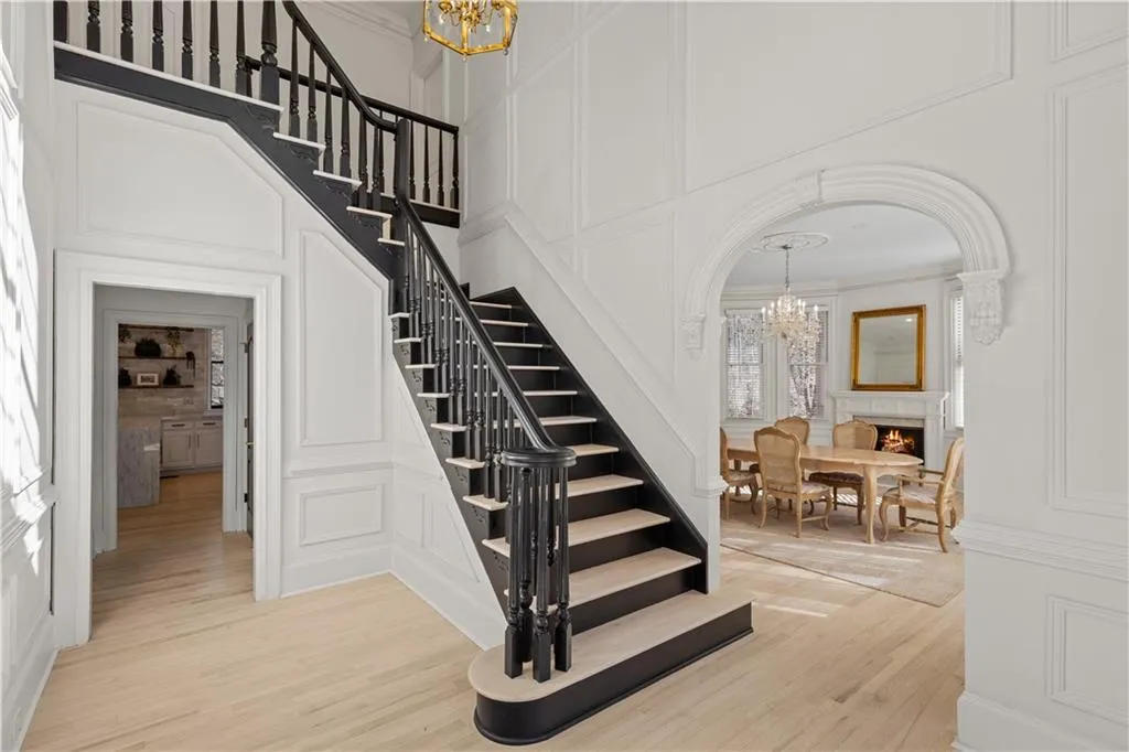 Stairs featuring a chandelier, a decorative wall, wood finished floors, crown molding, and a warm lit fireplace
