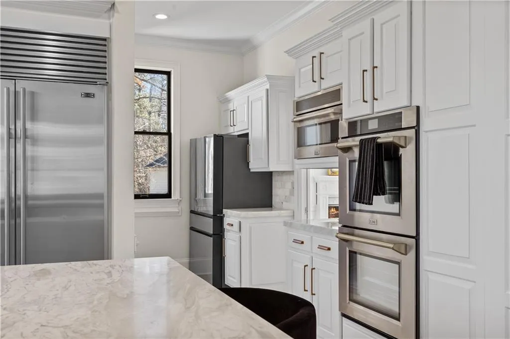 Kitchen with stainless steel appliances, crown molding, white cabinets, decorative backsplash, and light stone counters