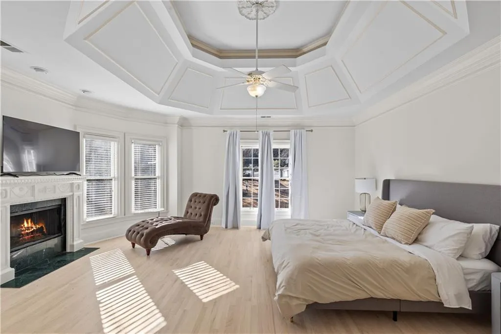 Bedroom with light wood-style floors, a fireplace, crown molding, ceiling fan, and multiple windows