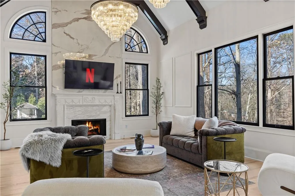 Living area with suspended lighting, a high end fireplace, lofted ceiling, light wood-type flooring, and a decorative wall