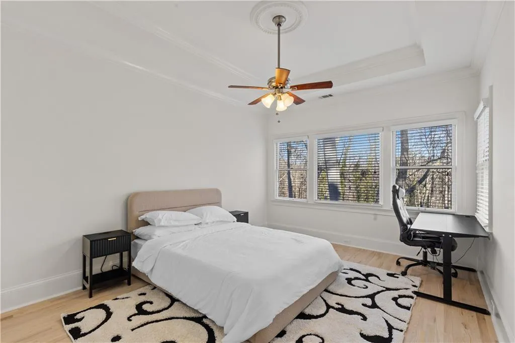 Bedroom with light wood finished floors, ceiling fan, a tray ceiling, and ornamental molding