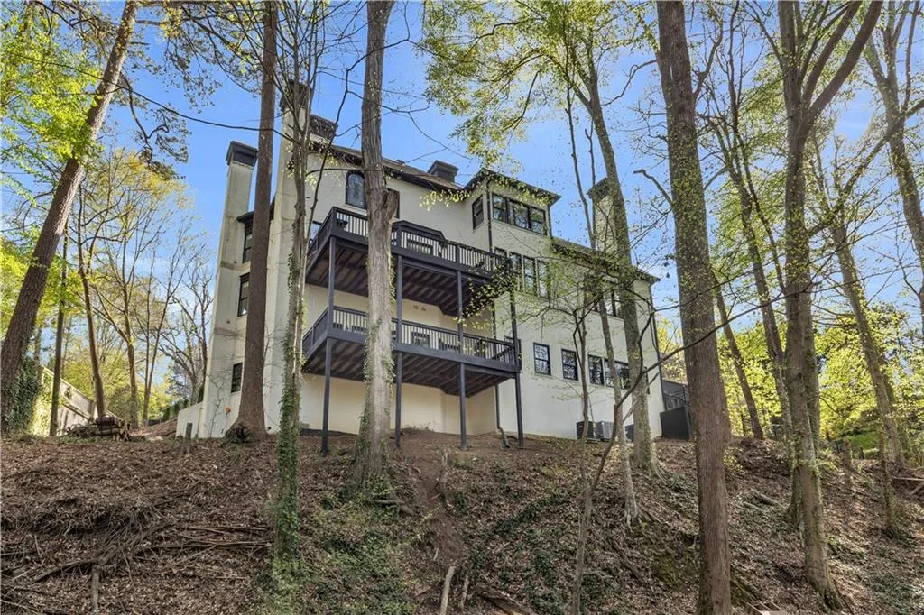 View of property exterior featuring stucco siding, a wooden deck, a chimney, and a balcony
