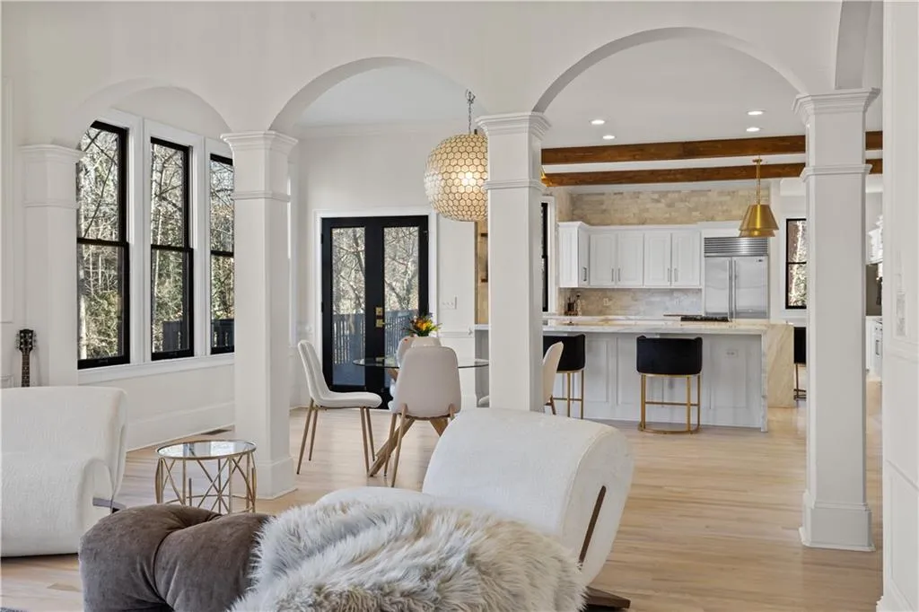 Living room featuring arched walkways, ornate columns, french doors, hanging lights, and beamed ceiling