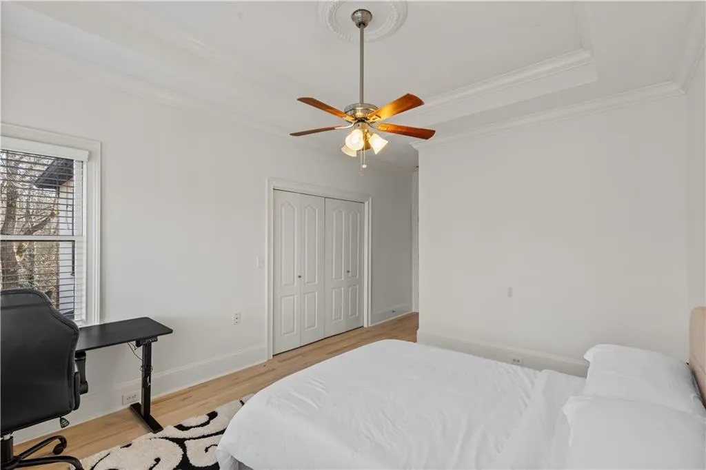 Bedroom featuring light wood-type flooring, crown molding, a ceiling fan, a tray ceiling, and a desk