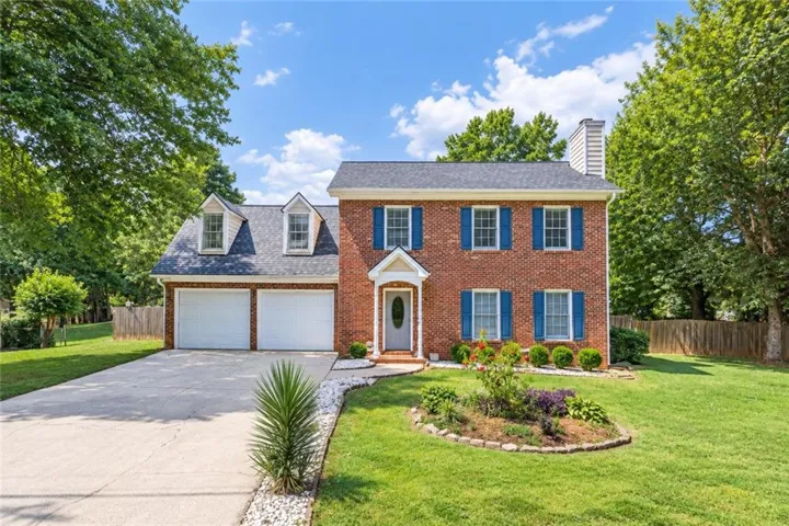 Brick exterior with blue window shutters, two-car garage, dormer windows, and a landscaped front yard