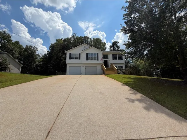 White exterior with black shutters, dual garage doors, and a wood staircase leading to the main entrance