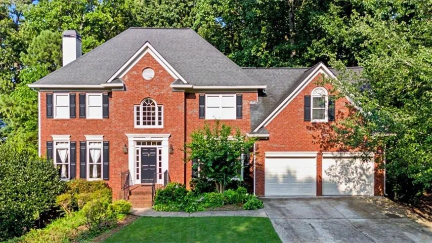 Brick facade residence featuring a prominent arched window, black shutter accents, a two-car garage, and a lush green lawn