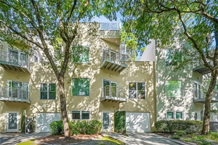 Modern multi-story facade featuring stucco exterior, numerous balconies with metal railings, integrated garage doors, and abundant natural light from large windows