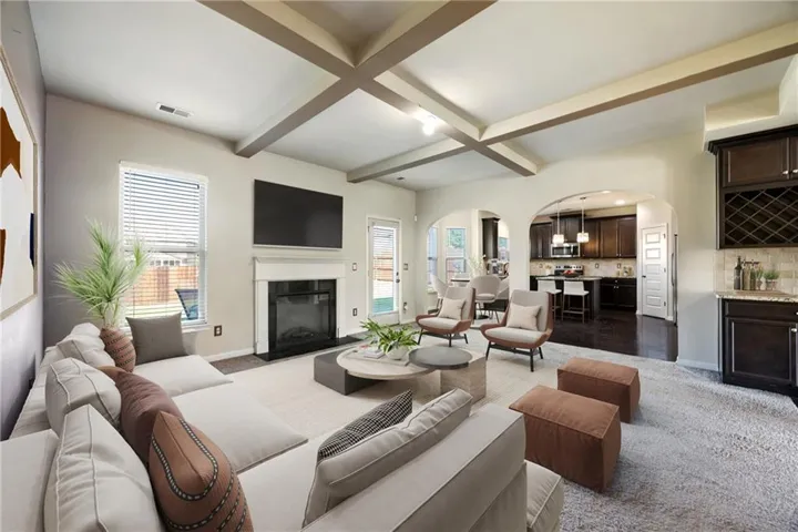Living room with arched walkways, beamed ceiling, dark colored carpet, coffered ceiling, and a fireplace with flush hearth