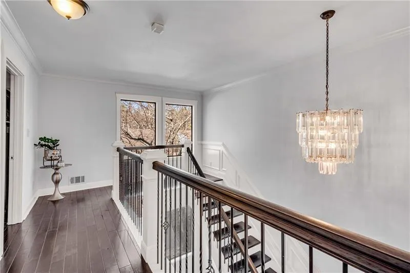 Hallway with dark wood-type flooring, ornamental molding, and an inviting chandelier