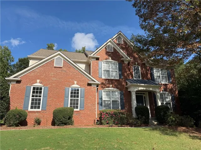 Brick exterior with white trim, covered front entry, gabled rooflines, multiple windows with shutters, and mature landscaping