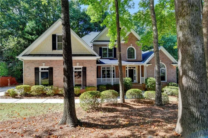 Brick facade with gabled roof lines, white columned porch, arched windows, and dark shutters