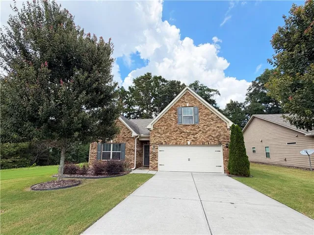 Brick facade home featuring an attached garage, concrete driveway, and mature landscaping