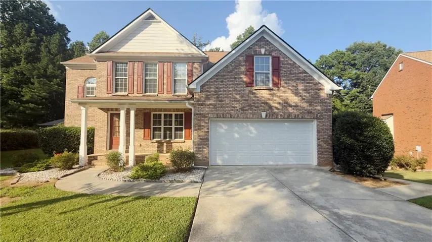 Brick facade with a two-car garage, covered porch, and mature landscaping
