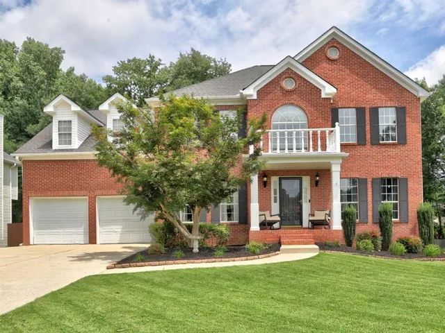 Brick exterior with white trim, two-car garage, covered entry porch, second-story balcony with balustrade, and manicured lawn